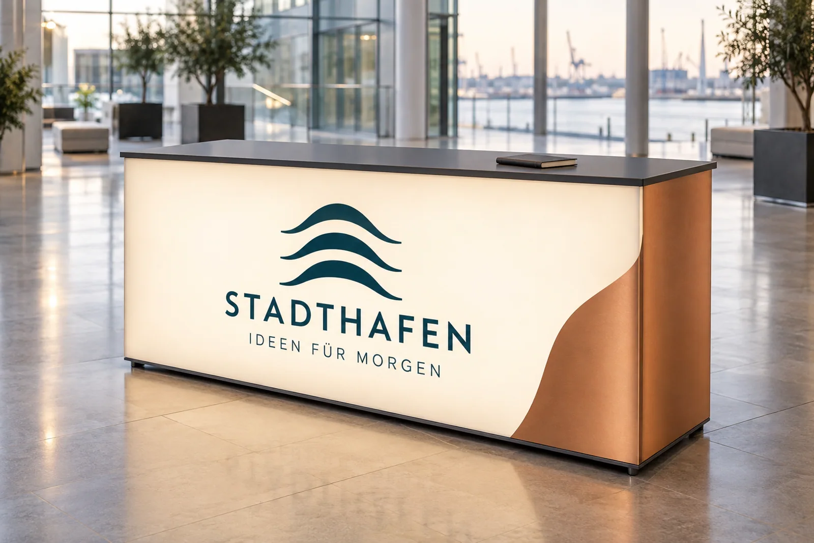 Beleuchtete Textiltheke mit STADTHAFEN-Wortmarke, petrolfarbenem Wellenlogo und kupferfarbener Seitenfläche in einem hellen Foyer.