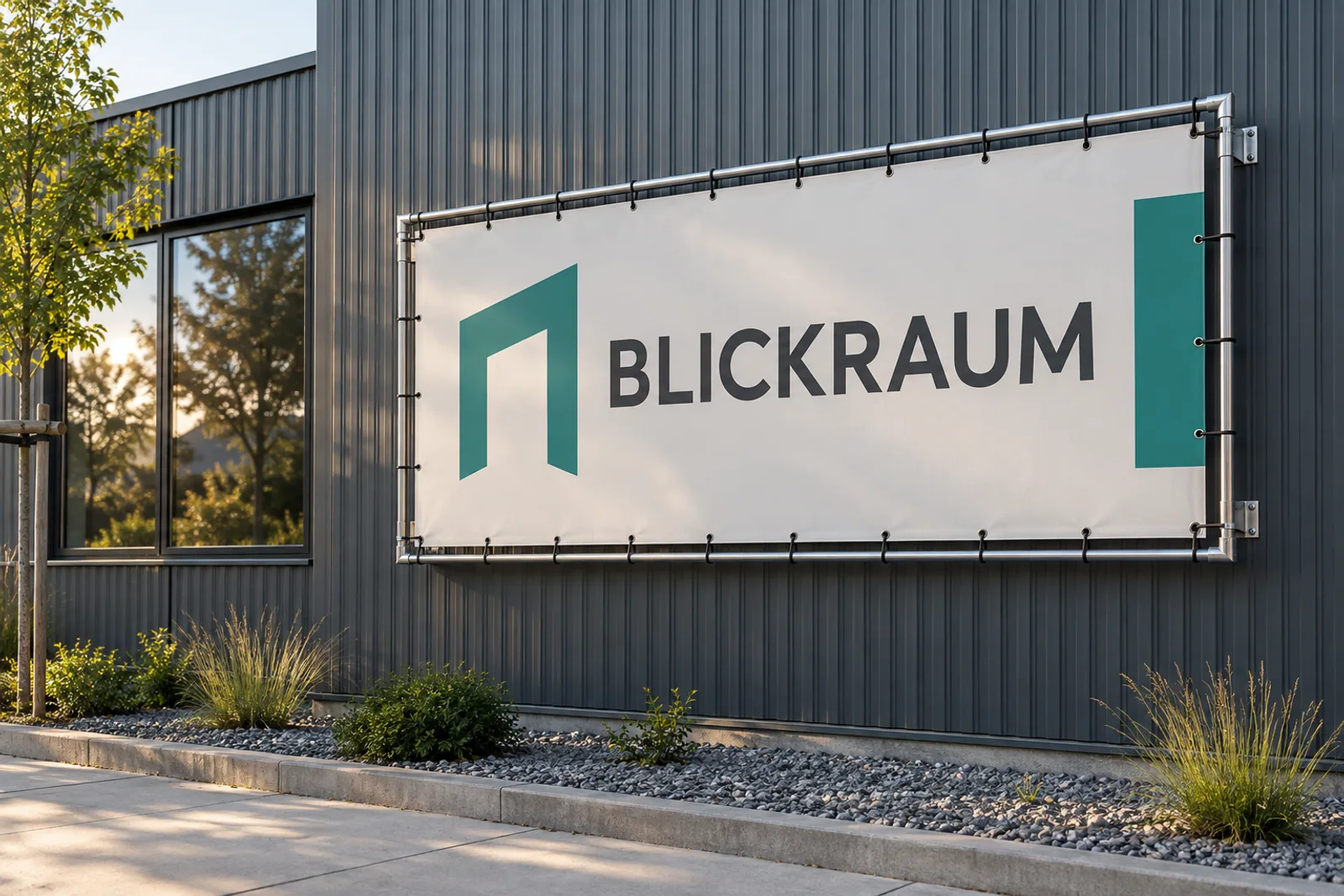 Helles BLICKRAUM-Banner mit türkisfarbenem Portalzeichen in einem wandmontierten Metallrahmen vor einer anthrazitfarbenen Gewerbefassade.
