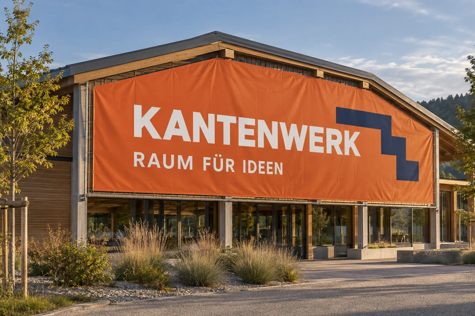Orangefarbenes Großformatbanner „KANTENWERK – RAUM FÜR IDEEN“ mit dunkelblauem Winkelsignet an der Giebelseite eines modernen Holzgebäudes.