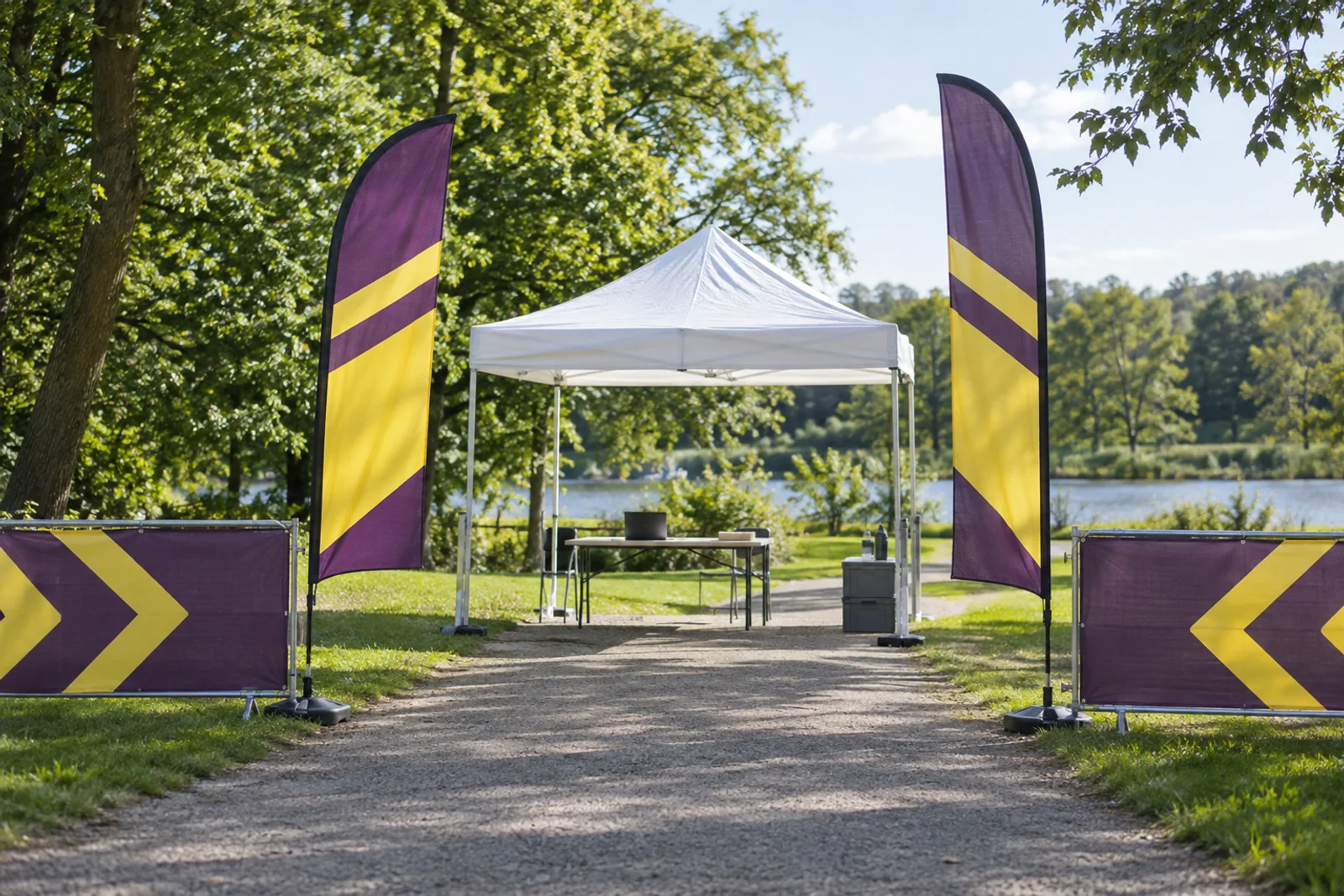 Weißer Veranstaltungspavillon zwischen violett-gelben Beachflags und passenden Absperrbannern in einem Park.