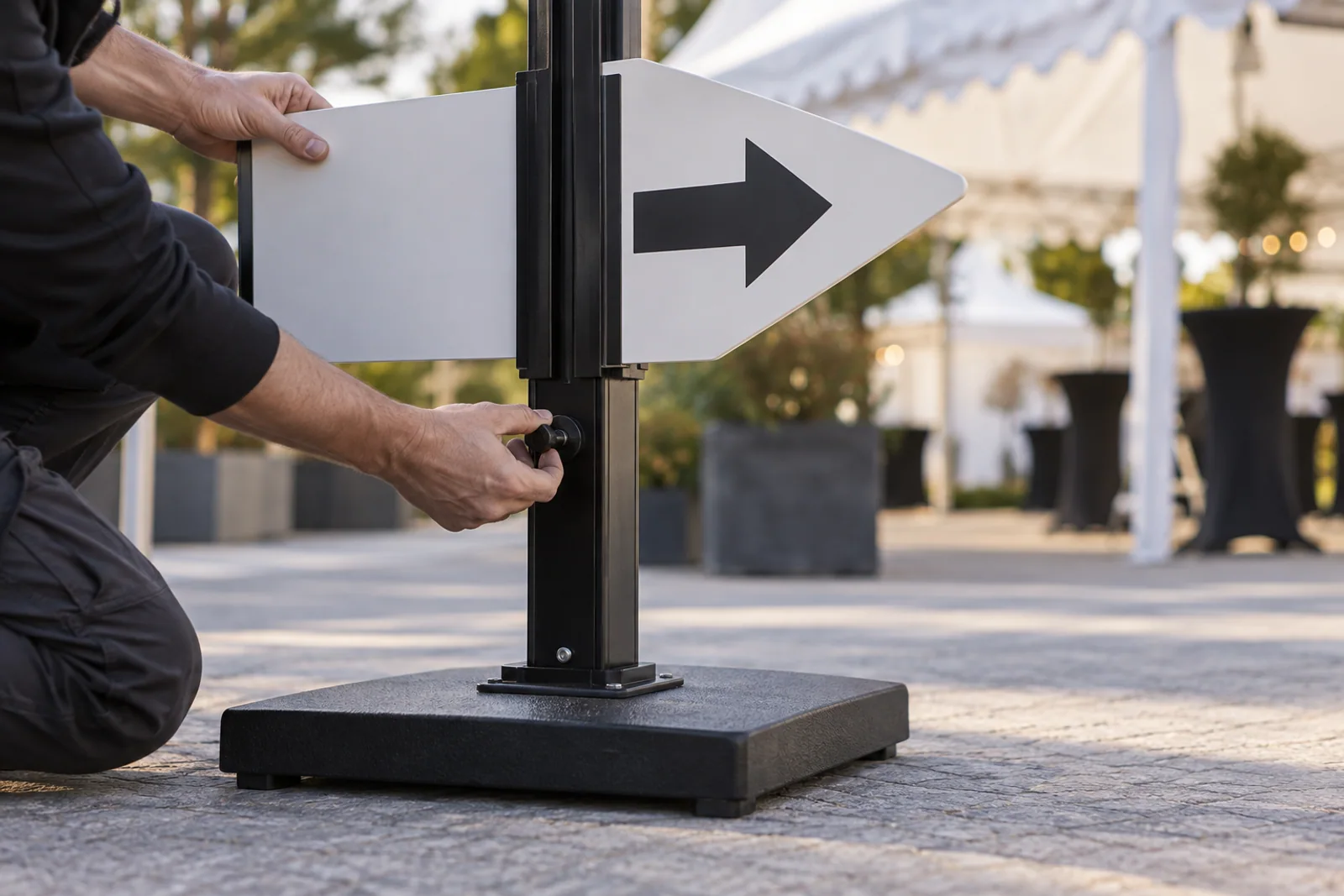 Ein Monteur befestigt eine Pfeiltafel an einem mobilen Wegweiser mit schwerem Standfuß.
