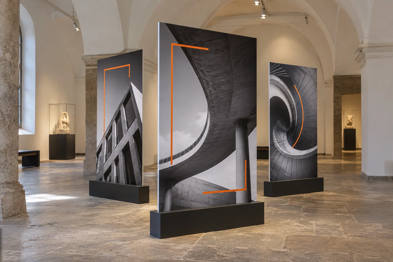 Drei freistehende bedruckte Ausstellungstafeln mit Architekturfotografien in einem Gewölberaum.