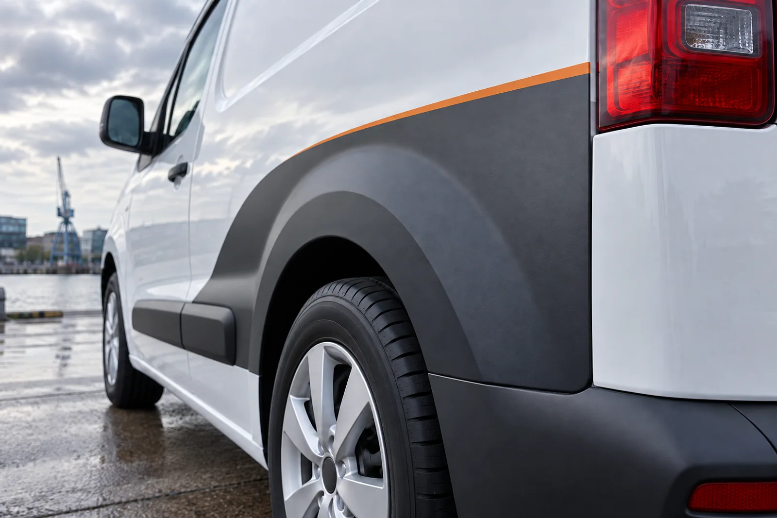 Detail einer anthrazitfarbenen Teilfolierung mit orangefarbener Linie am hinteren Radlauf eines weißen Transporters.