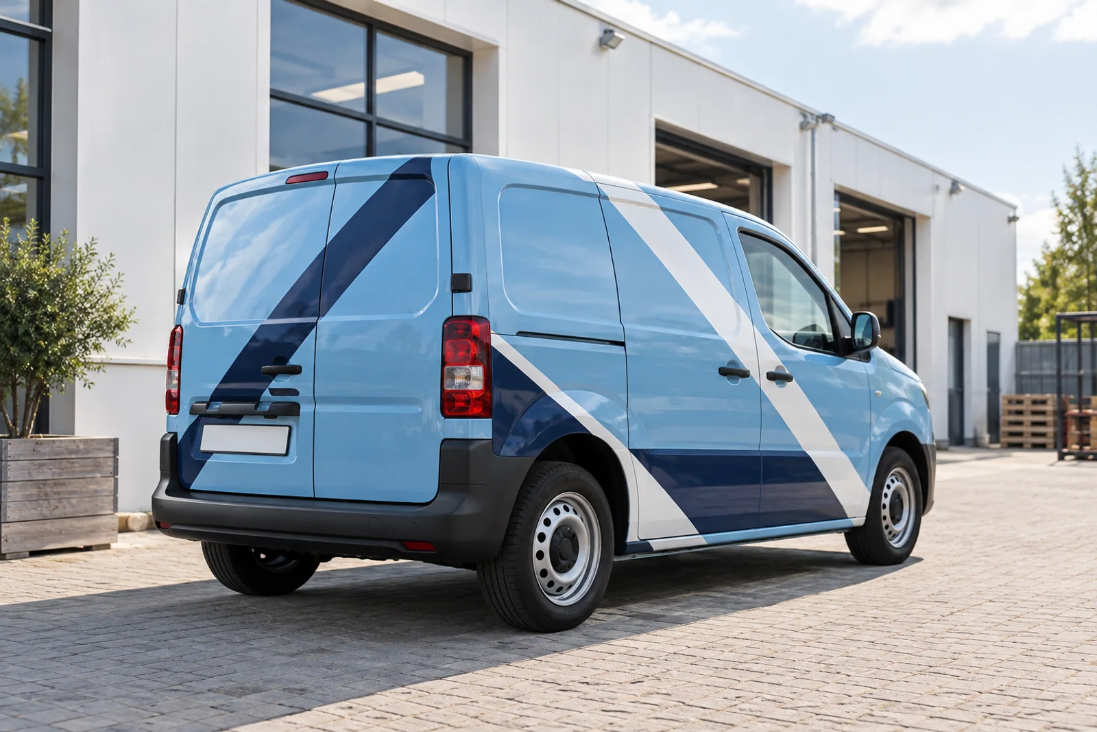 Hellblauer Service-Transporter mit weißen und dunkelblauen Diagonalstreifen vor einer Werkstatt.