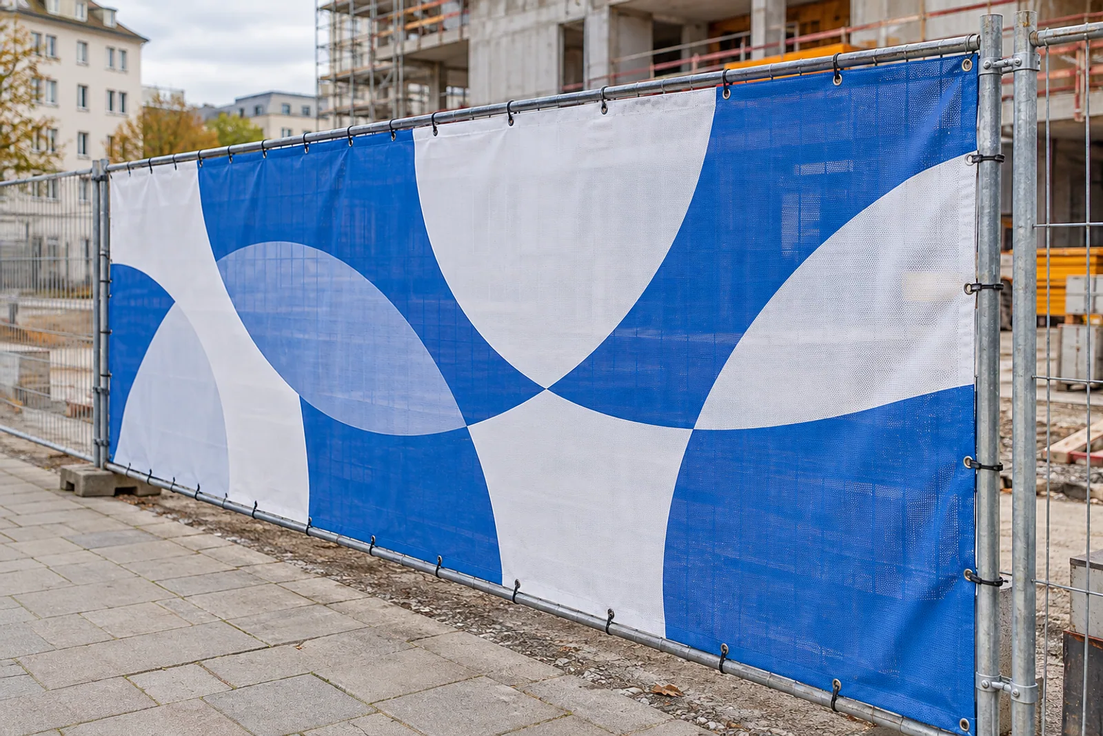 Blau-weiß bedrucktes Meshbanner mit Ösen und Spannschlaufen an einem Bauzaun.