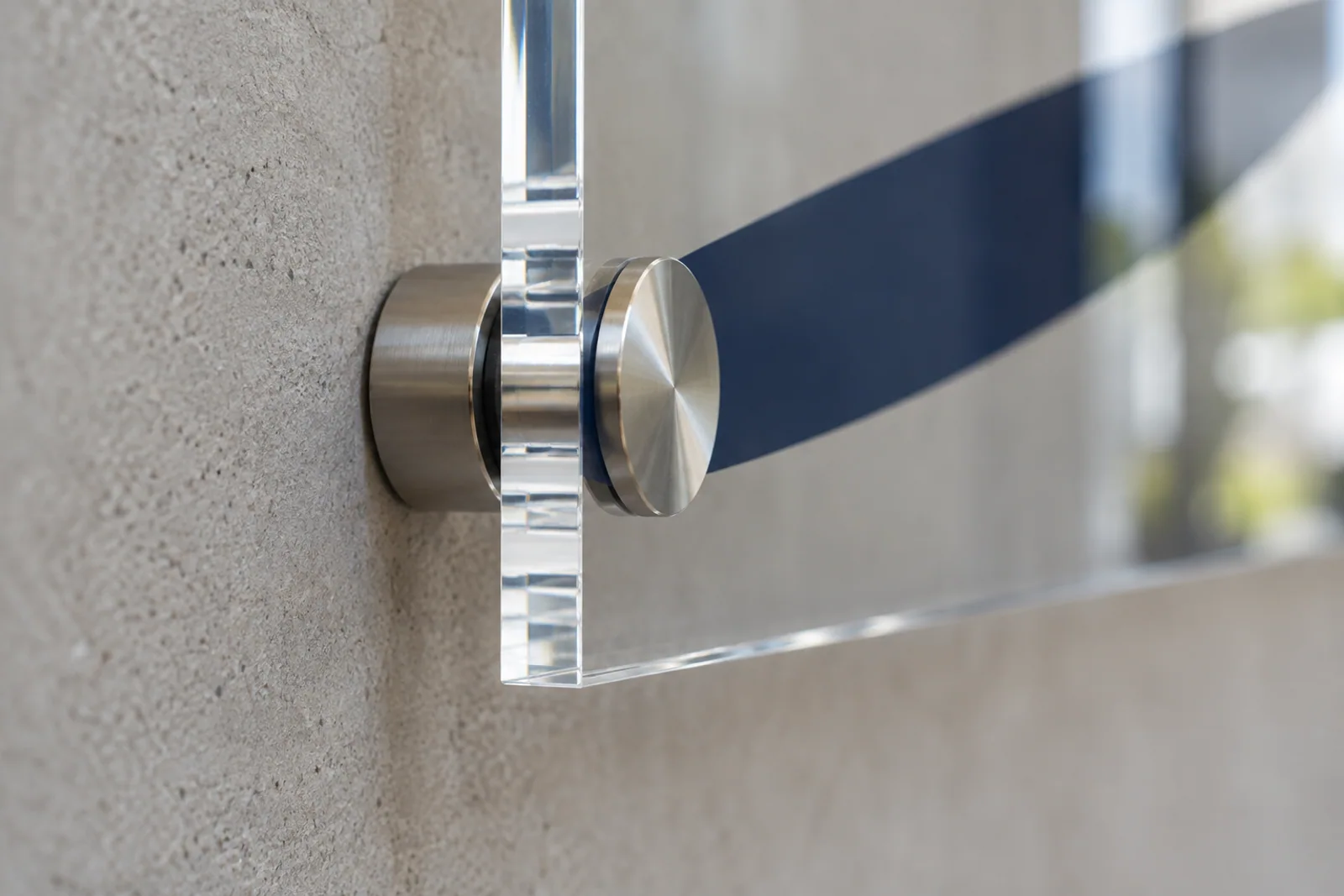 Seitliche Nahaufnahme einer transparenten Acrylplatte mit Metall-Abstandshalter vor einer hellen Wand.